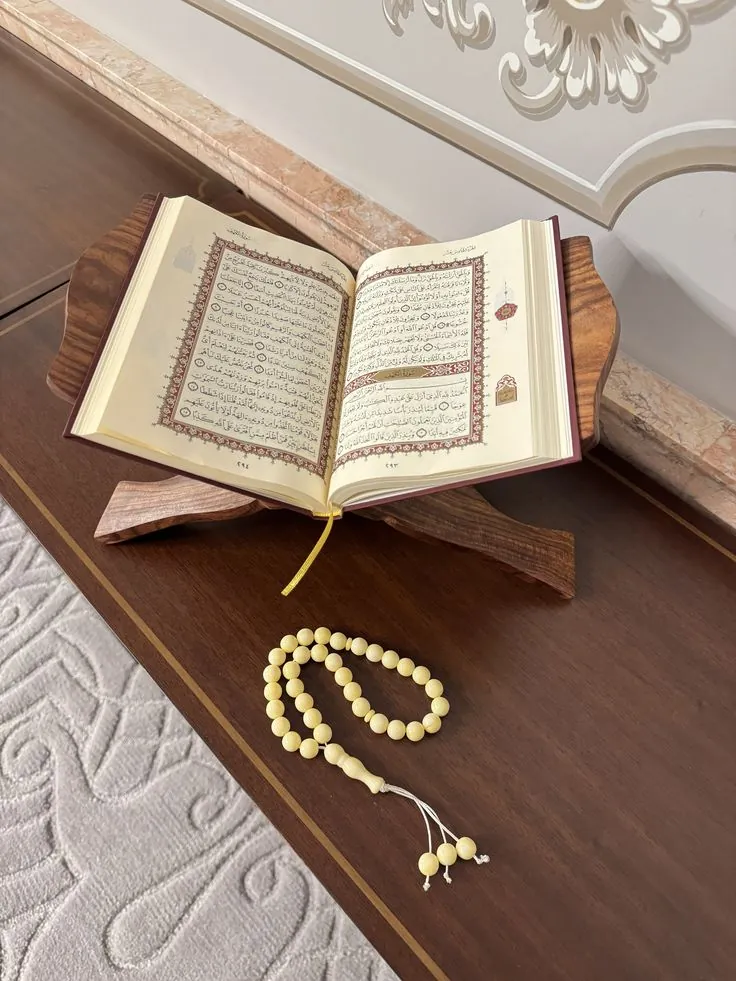 An open Qur'an on a wooden stand with a string of prayer beads