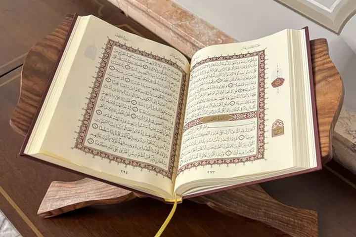 An open Qur'an on a wooden stand beside prayer beads